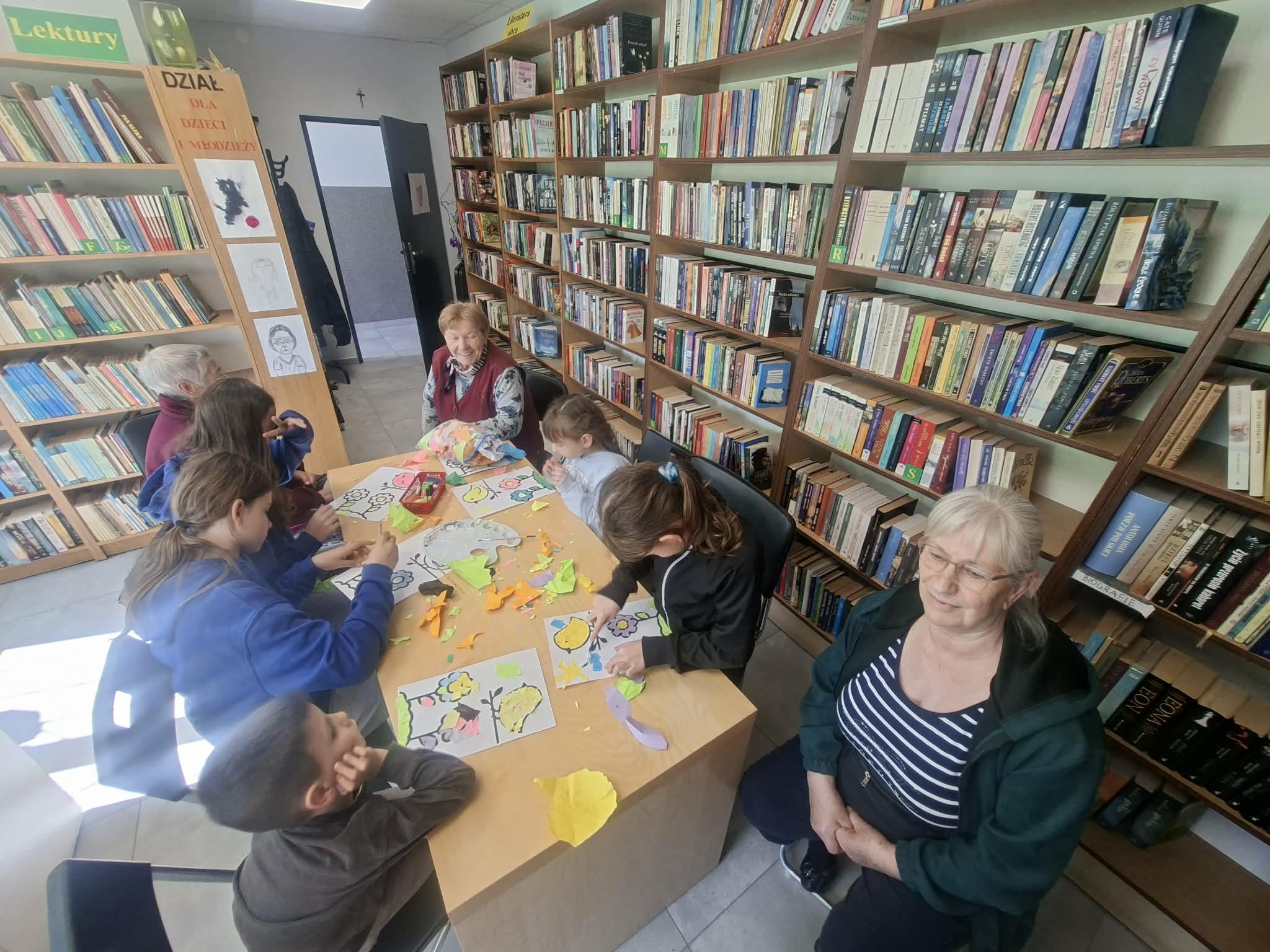 grupa dorosłych i dzieci siedzi przy stole i tworzą prace plastyczne