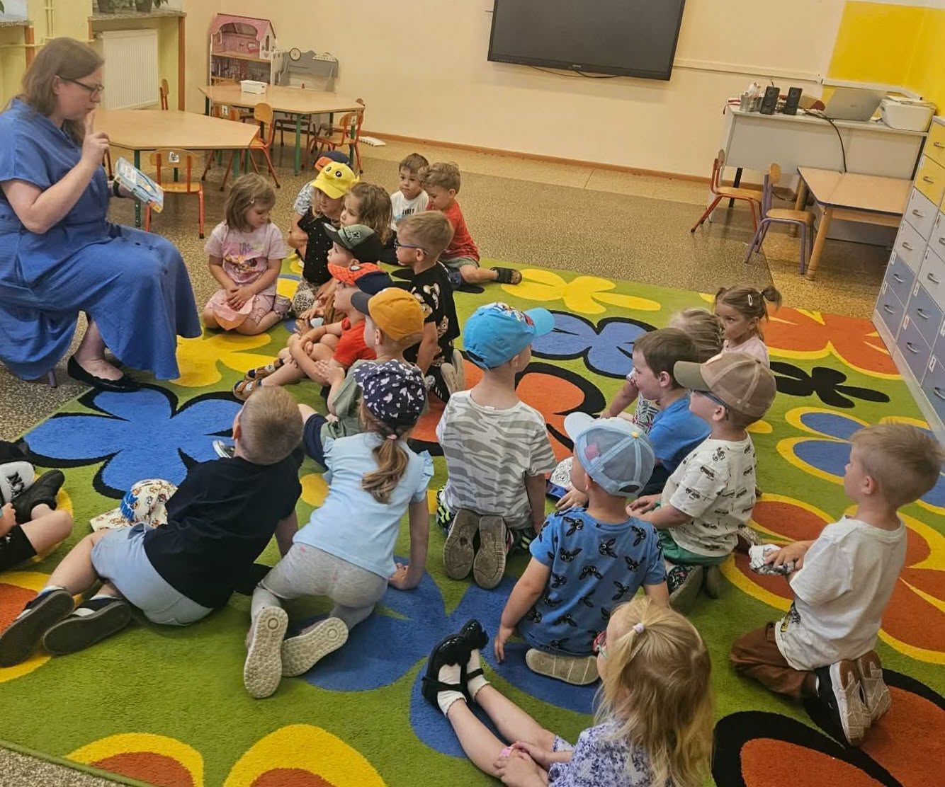 pani bibliotekarka czyta książkę grupie dzieci siedzącej na dywanie