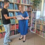 pani z biblioteki wręcza wolontariuszowi dyplom i słodkie podziękowanie